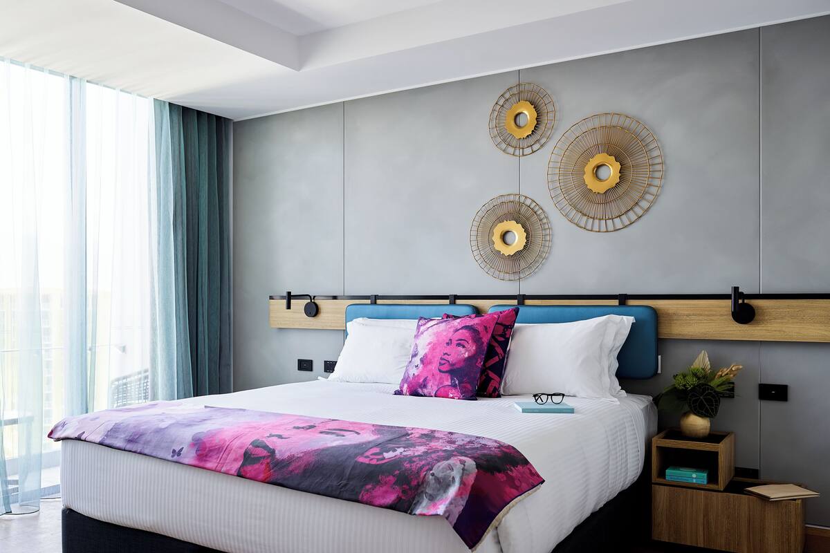 A modern bedroom with a large bed, a headboard with built-in speakers, and decorative wall art.
