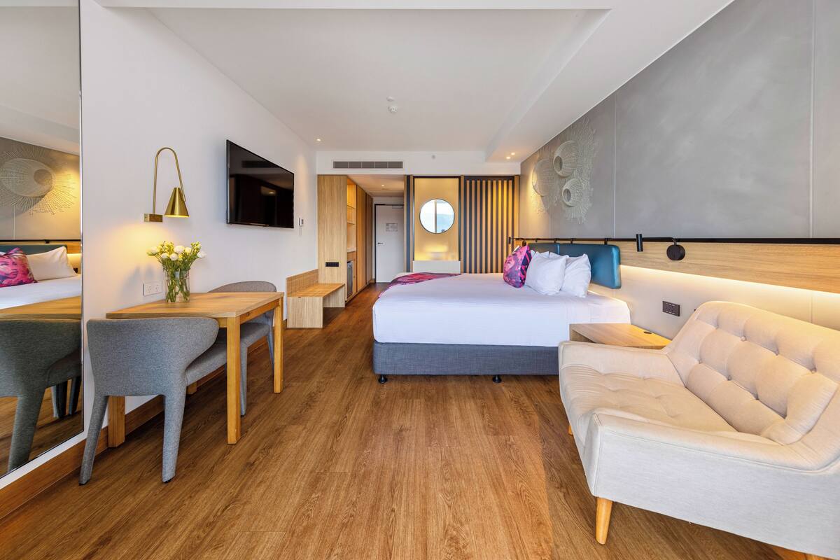 A modern hotel room with a bed, a desk, a chair, and a TV.