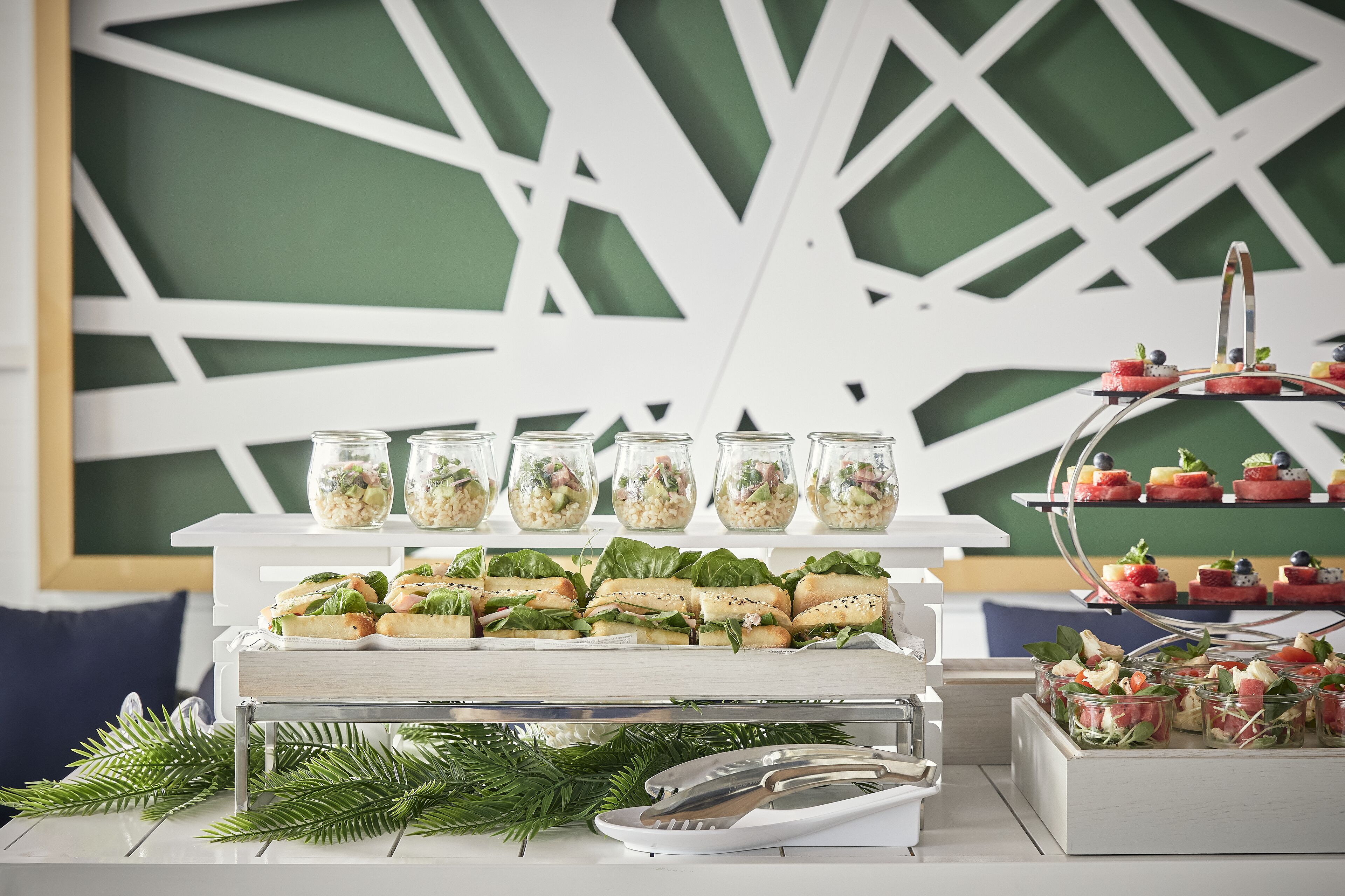En buffet med sandwiches, salater og desserter præsenteret på forskellige niveauer.
