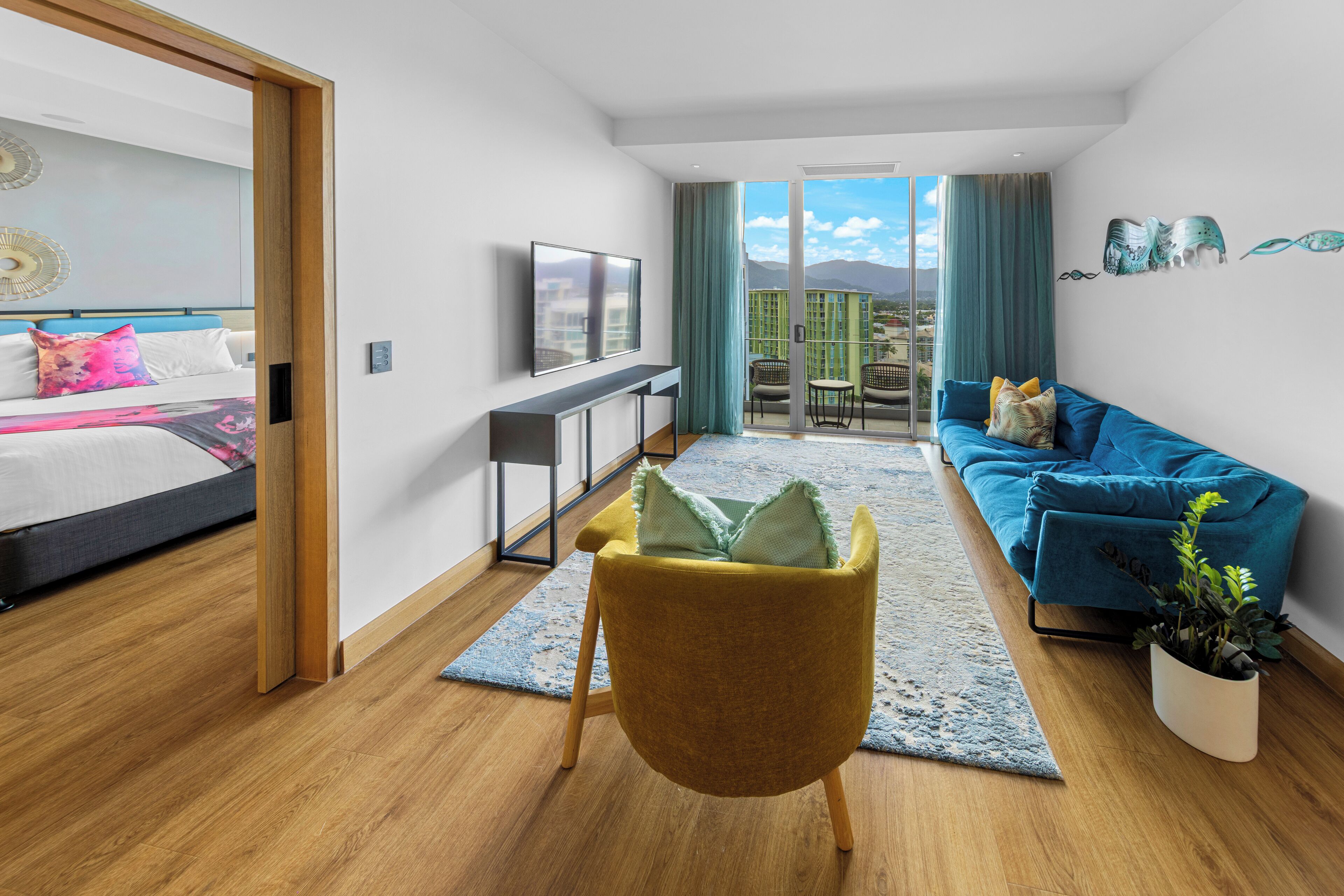 A modern hotel room with a bed, a sofa, a TV, and a balcony with a view.