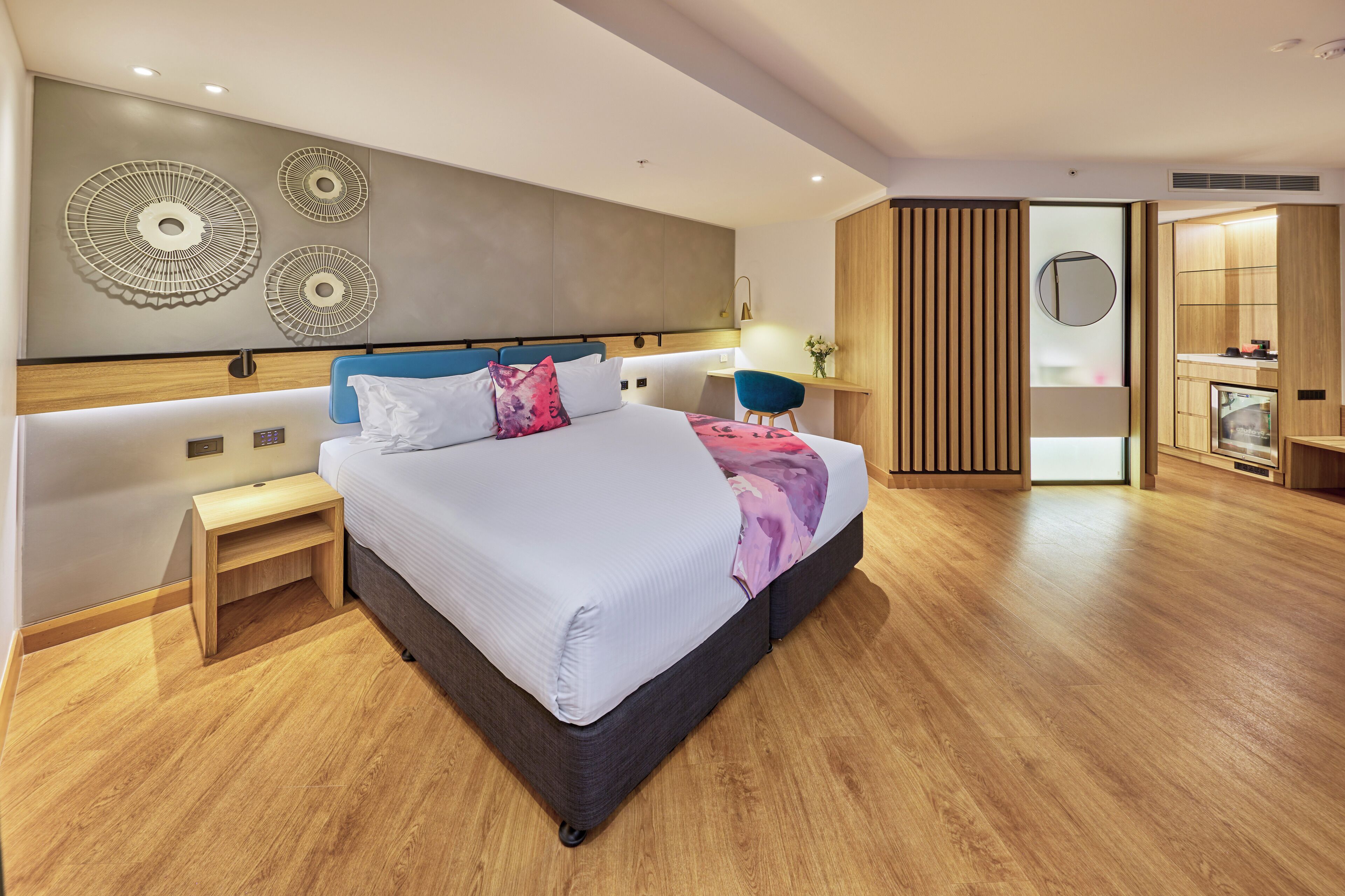 A modern hotel room with a large bed, bedside tables, a desk, and a wardrobe.
