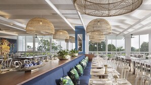 A restaurant with a long blue bench, white chairs, and hanging rattan lamps. - Crystalbrook Flynn (Cairns)