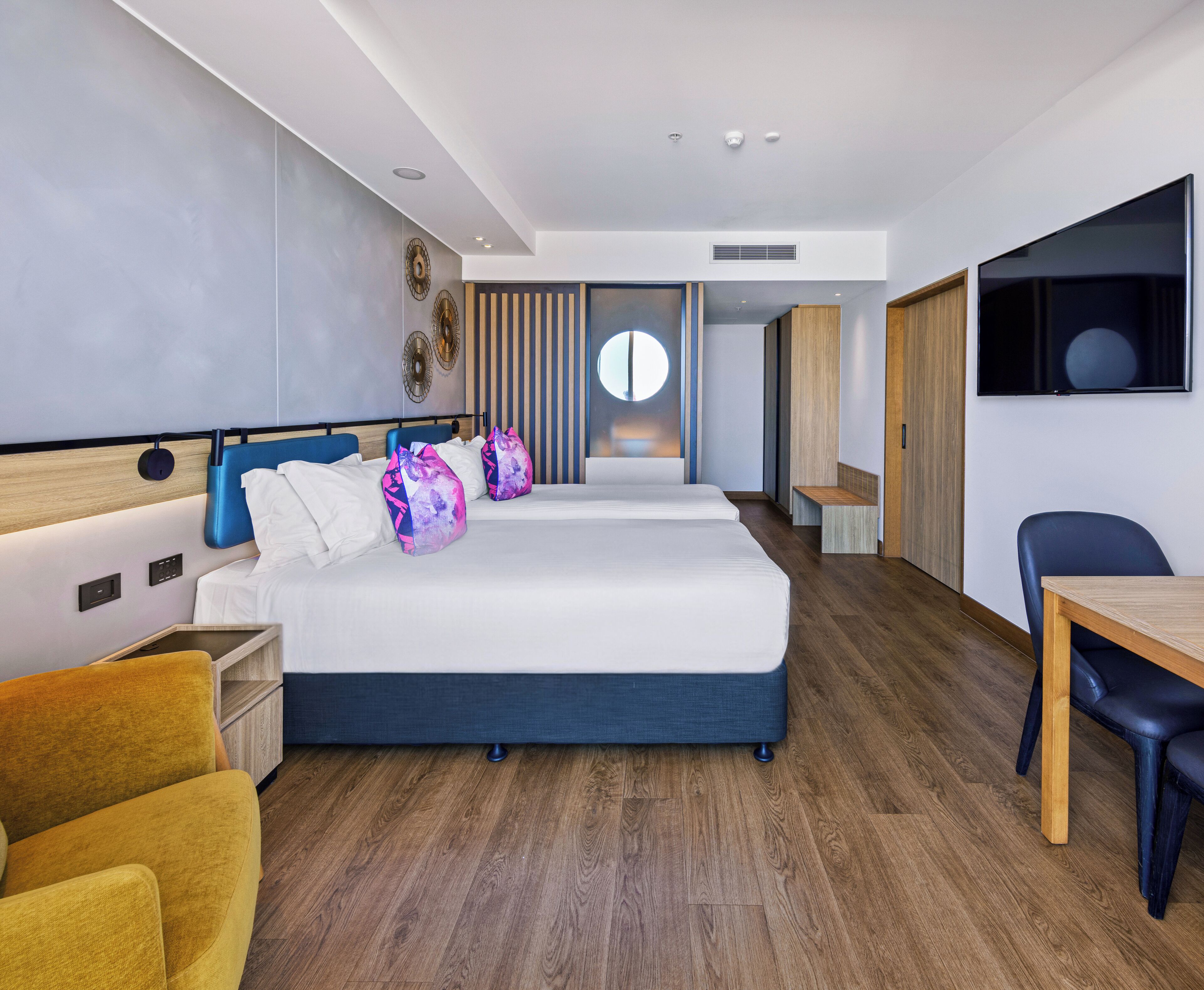 A modern hotel room with a large bed, a desk, a chair, and a TV.