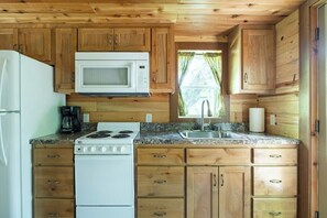Una cocina compacta con armarios de madera, estufa blanca, microondas y un lavamanos.