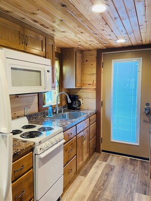 A compact kitchen with a microwave, stove, sink, and wooden cabinets. - Sleepin Bear Treehouse - Private Hot Tub (Guild)