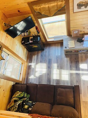 Interior acogedor de una cabaña con techo de madera, televisor de pantalla plana, estantería y una ventana.