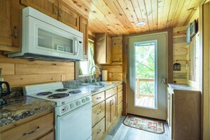 A compact kitchen with wooden cabinetry, a white stove, a microwave, and a sink. - Sleepin Bear Treehouse - Private Hot Tub (Guild)