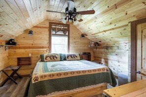 Camera da letto in una baita di legno, con un letto, una ventola a soffitto, una finestra con tende e una porta.