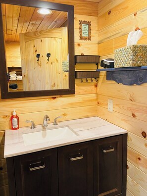 Un interno in legno con uno specchio grande, un lavabo con due rubinetti e uno scaffale con articoli da toilette.