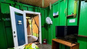 Ein Zimmer mit einem Bett, einem Fernseher, einem Ventilator und einer Tür, die nach draußen führt.