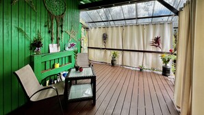 Eine grüne Holzdachterrasse mit einem Glastisch und Stühlen, umgeben von Blumentöpfen und Dekorationselementen.