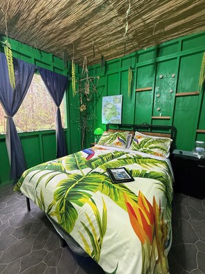Ein Zimmer mit grünen Wänden, einem Bett mit Bettwäsche mit tropischem Muster, einer Karte an der Wand und einer sternförmigen Wanddekoration.