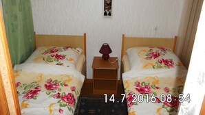 Ein Zimmer mit zwei Betten, jeweils mit floralem Bettzeug, einem kleinen Nachttisch mit Lampe und einem Bild an der Wand.