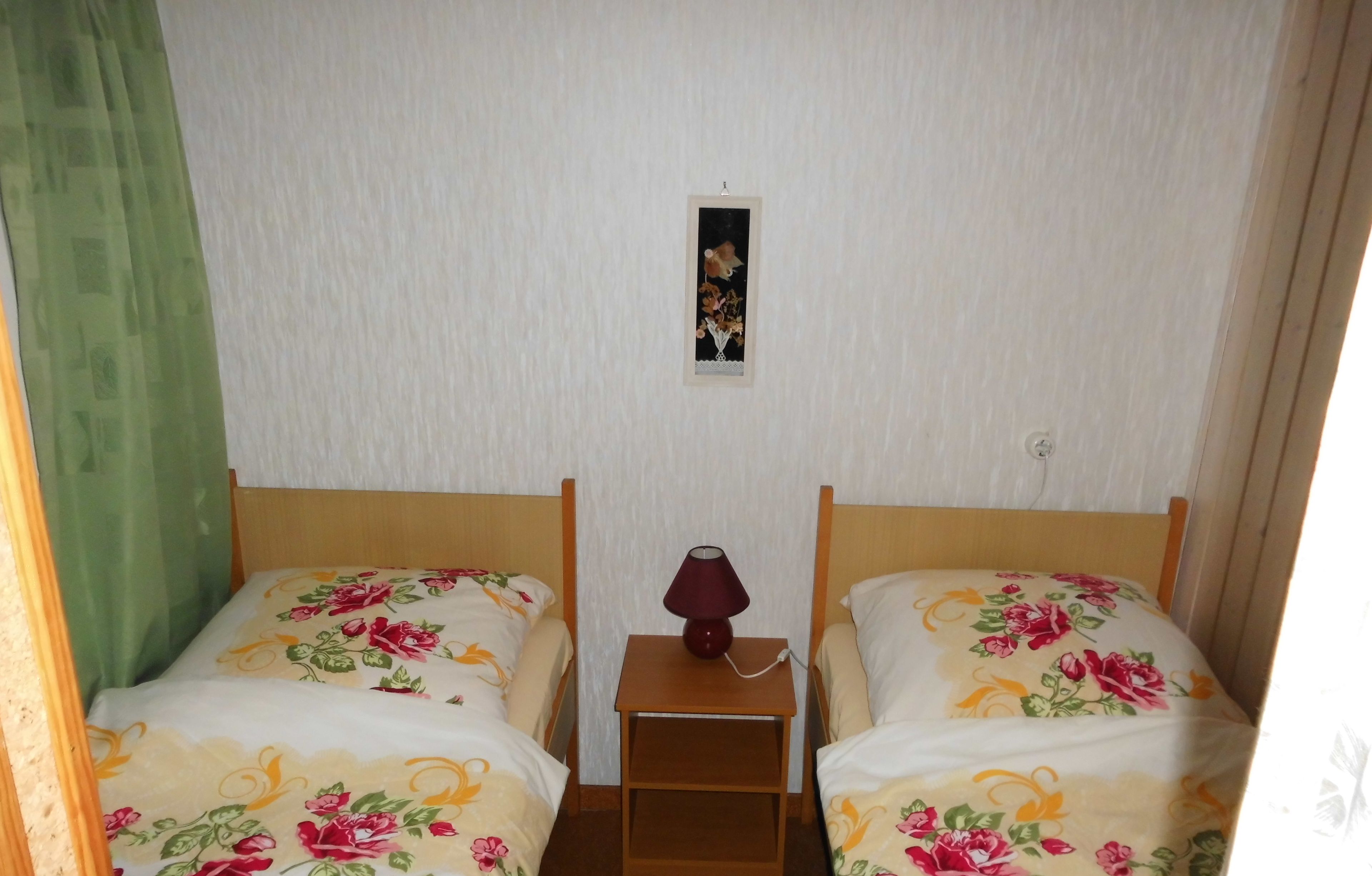 Ein Zimmer mit zwei Betten, jeweils mit floralem Bettzeug, einem kleinen Nachttisch mit Lampe und einem Bild an der Wand.