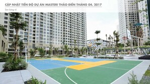Un terrain de basket avec une surface de jeu aux couleurs verte, bleue et jaune, entouré de palmiers et d’immeubles modernes.