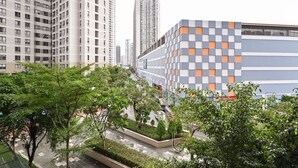 Un bâtiment moderne à la façade géométrique, entouré de verdure et situé à proximité d’immeubles résidentiels de grande hauteur.
