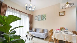 Un salon chaleureux avec un canapé, une table à manger et des chaises. On y trouve un lustre, des rideaux et des œuvres d’art mural.