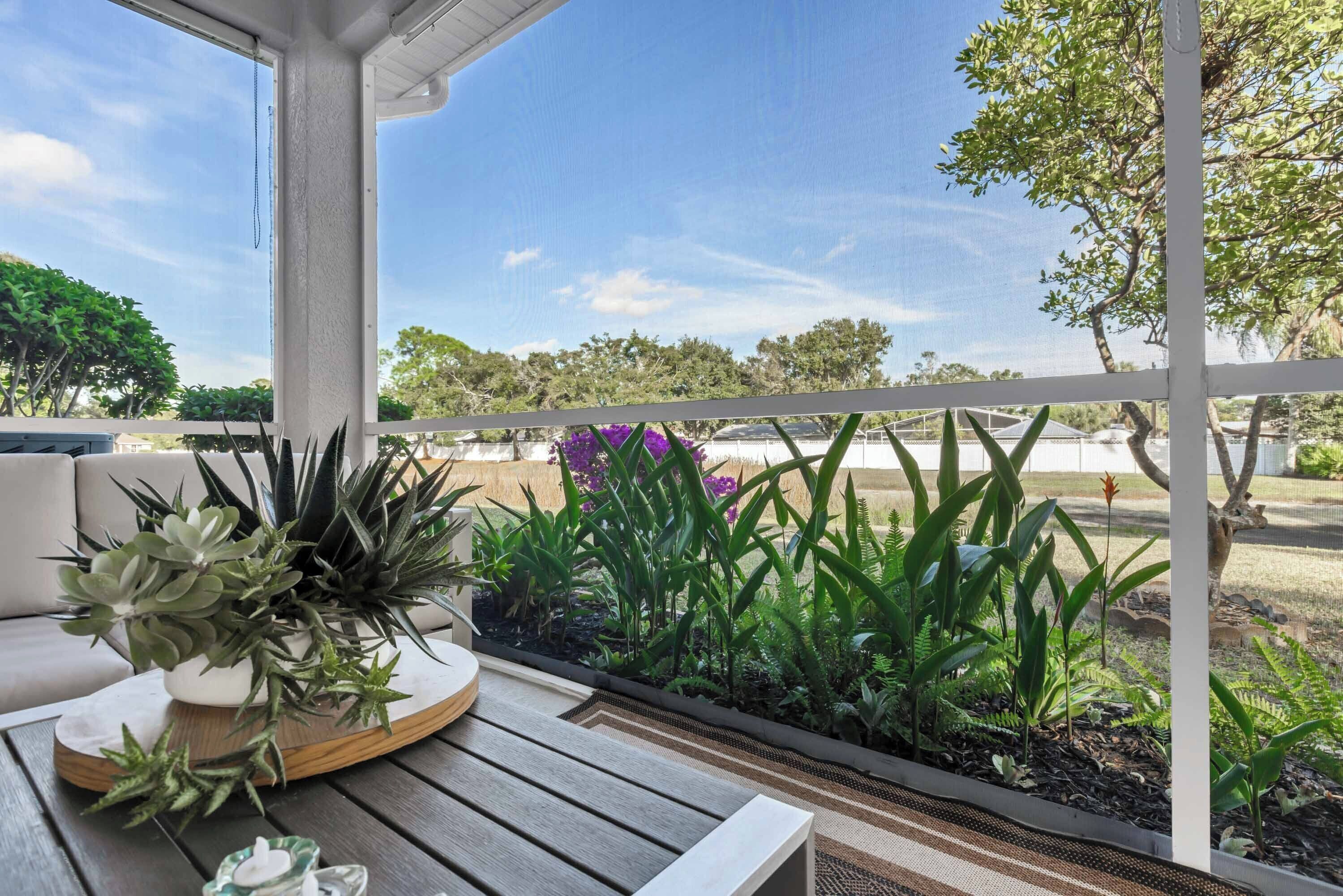 A covered outdoor seating area with a wooden table, potted plants, and a view of the surrounding landscape.