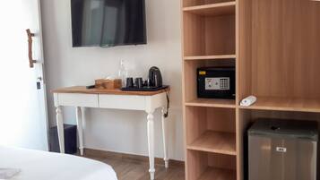 A hotel room with a wooden desk, a television mounted on the wall, a minibar, and a bed.