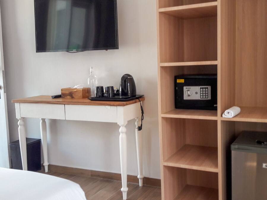 A hotel room with a wooden desk, a television mounted on the wall, a minibar, and a bed.