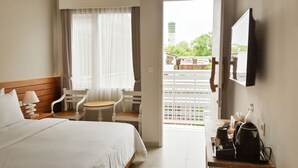 A hotel room with a bed, a desk with a coffee maker, a TV, and a window with curtains. - Mantra Gili (Gili Trawangan)