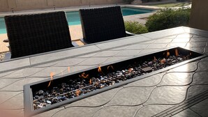 Une terrasse extérieure avec une table en pierre et deux chaises en osier, donnant sur une piscine.