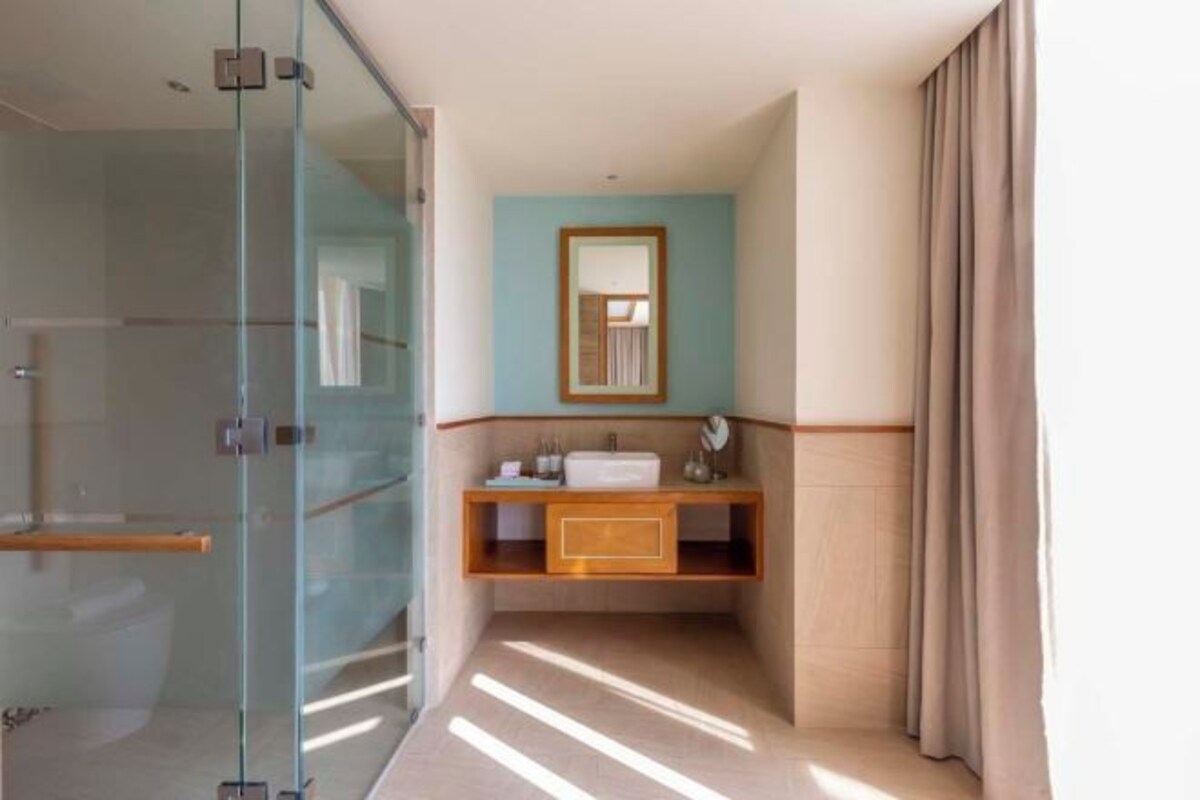A bathroom with a glass shower enclosure, a wooden vanity, a mirror, and a beige curtain.