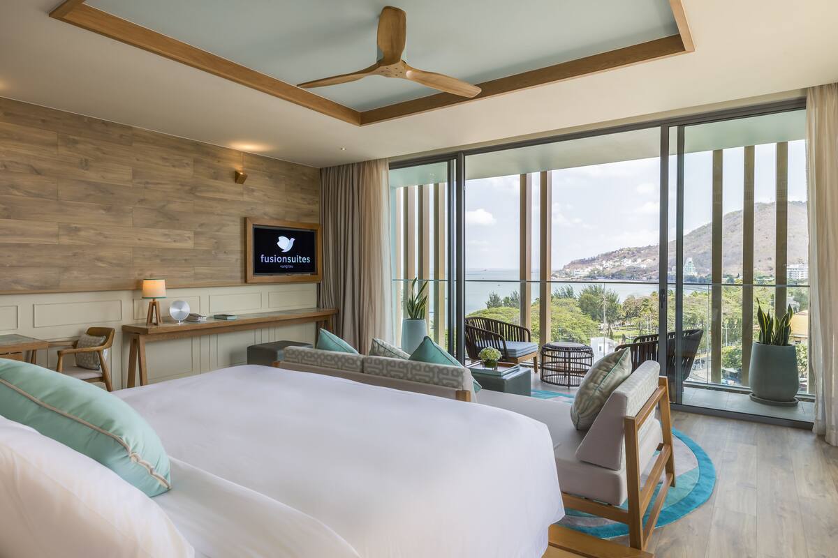 Habitación de hotel moderna con una cama grande, un escritorio, un televisor y un balcón con vistas a la ciudad.