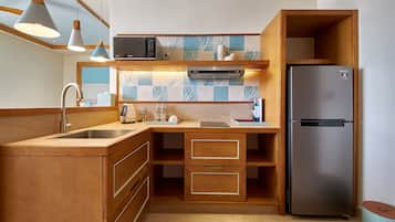 A compact kitchen with wooden cabinetry, a stainless steel refrigerator, a microwave, and pendant lights.