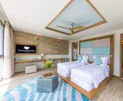 A modern hotel room with a wooden ceiling, two beds, a desk, and a TV displaying 'fusionsuites'.