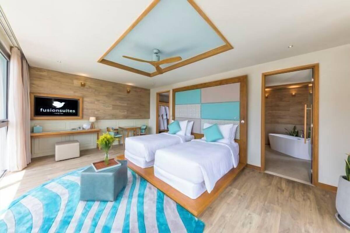 Una habitación de hotel moderna con dos camas, un ventilador de techo, un televisor, un baño y piso de madera.