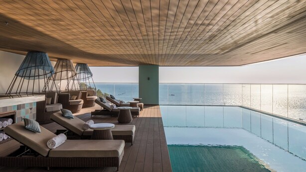 A sunlit outdoor lounge area with wooden flooring, lounge chairs, and a pool. - Fusion Suites Vung Tau (Ho Chi Minh City)