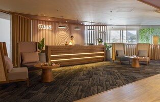 Una zona de recepción con un mostrador de madera, dos recepcionistas y arreglos de asientos que incluyen sofás y sillones.