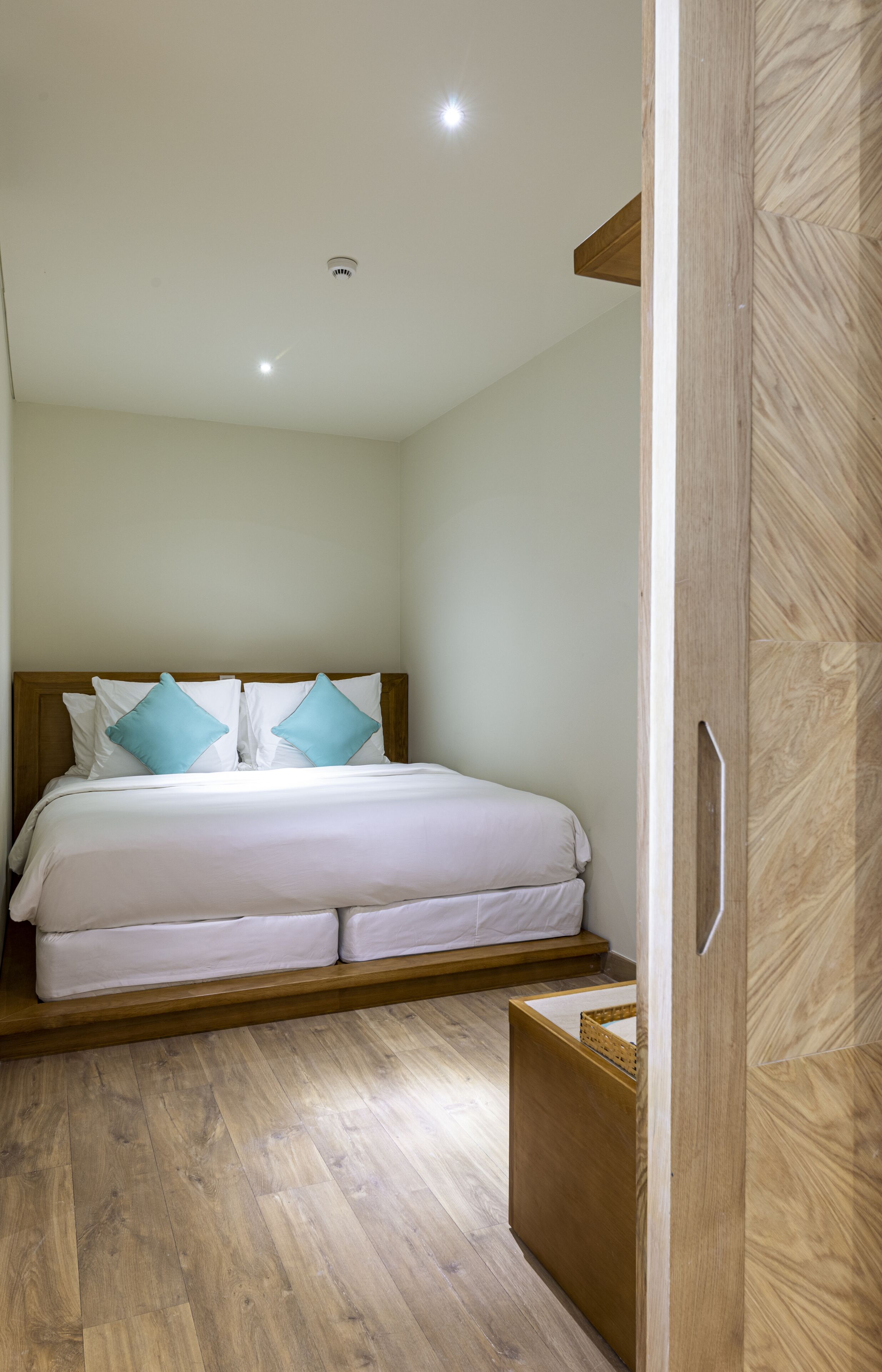 A neatly made bed with white bedding and two blue pillows, a wooden headboard, and a wooden floor.