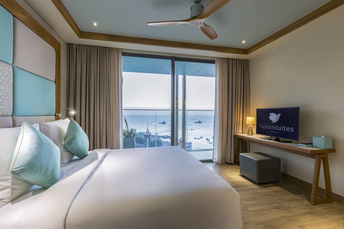 Una habitación de hotel con una cama grande, televisión, escritorio y vista al océano.
