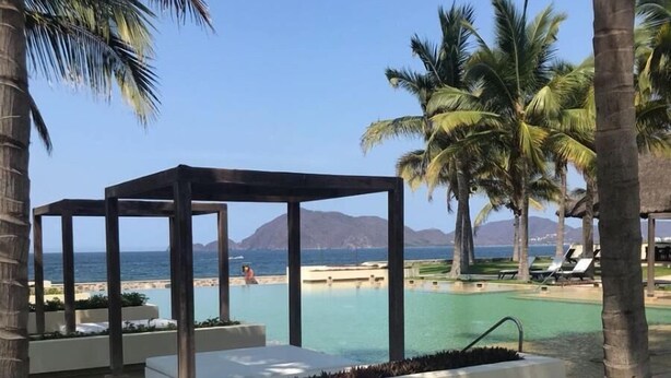 Ein Poolbereich mit Liegestühlen, einer Pergola und Palmen.