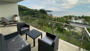 Ein Balkon mit Korbmöbeln, Blick auf den Strand und Palmen.