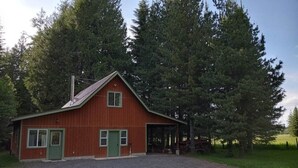 Une grange rouge avec une porte et des fenêtres vertes, entourée de grands arbres.