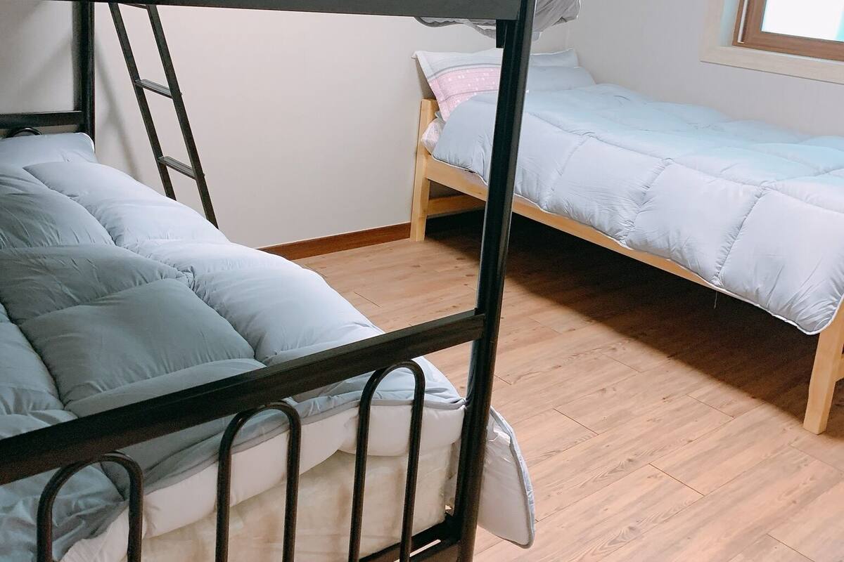 Une chambre avec un lit superposé, une échelle, un plancher en bois et une fenêtre.