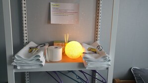 Hotelkamer met een plank met handdoeken, een rol toiletpapier, een decoratieve lamp en een bord met informatie over de kamer.