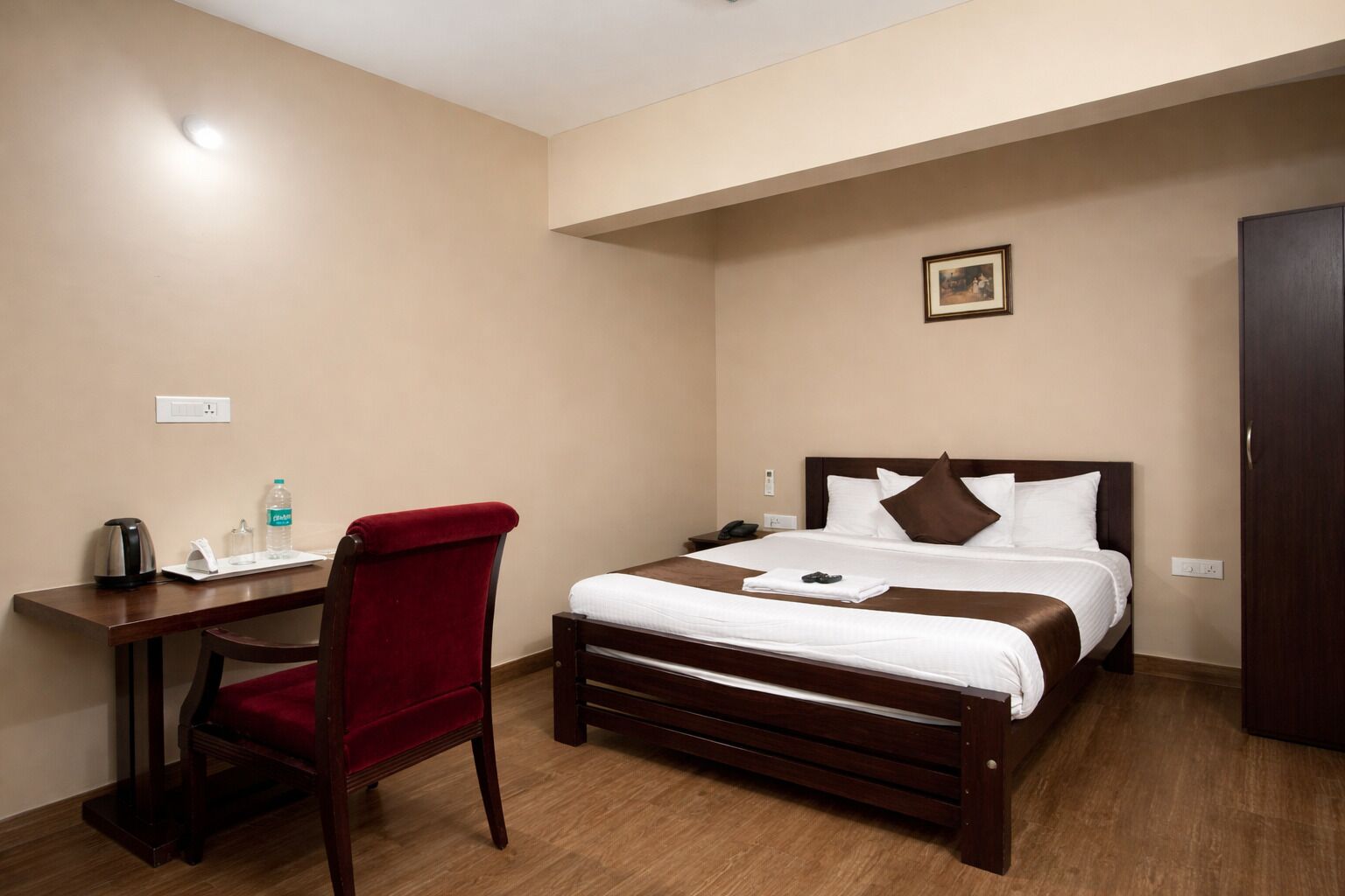 Een hotelkamer met een bed, een bureau, een stoel, een nachtkastje en een kledingkast.