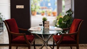 Een kamer met een glazen tafel, twee rode stoelen, een kleine plant en een menukaart op tafel.