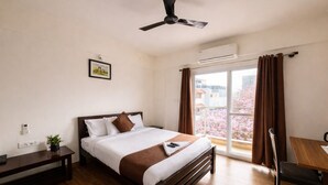 Hotelkamer met een bed, een bureau, een stoel, een plafondventilator, een airconditioner en een raam met gordijnen.
