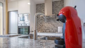A modern kitchen with granite countertops, stainless steel appliances, and a red kettle.