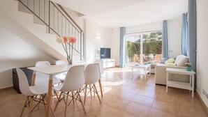 A modern living room with a dining area, a staircase, and a large window with curtains.