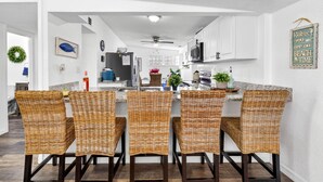 A modern kitchen with white cabinetry, a central island with wicker chairs, and a ceiling fan. - New Port Richey Downtown 🌴 (New Port Richey)