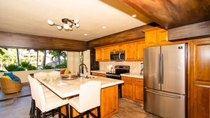A kitchen with wooden cabinets, a stainless steel refrigerator, a dining area with a white table and chairs, and a view of palm trees outside. - Marina Sol Condominiums (Cabo San Lucas)