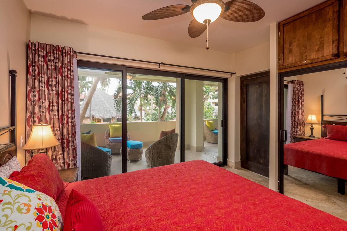 A hotel room with a bed, a balcony with wicker furniture, and a ceiling fan.