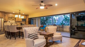 A modern kitchen with wooden cabinets, a dining area with bar stools, and a living room with a sofa and armchairs. - Marina Sol Condominiums (Cabo San Lucas)