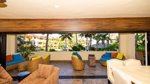 A spacious outdoor seating area with wicker furniture and colorful cushions, overlooking a pool and palm trees. - Marina Sol Condominiums (Cabo San Lucas)